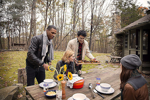 Männer,  die Freunden am Tisch an Bäumen sitzend Essen servieren