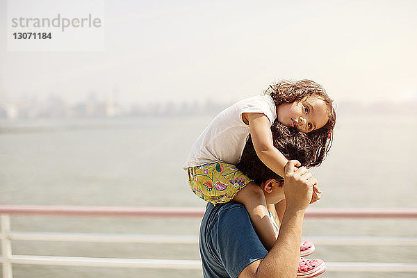 Seitenansicht eines Vaters,  der seine Tochter auf der Schulter gegen den Himmel trägt