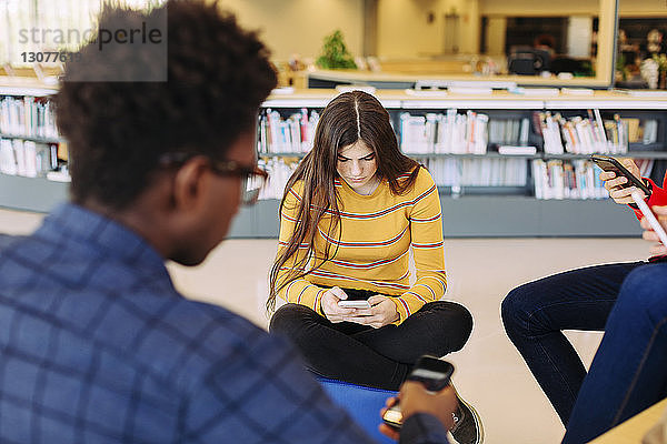 Freunde benutzen Smartphones,  während sie in der Bibliothek sitzen