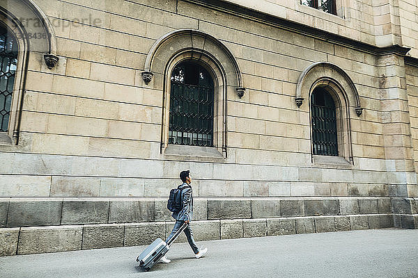 Seitenansicht eines Geschäftsmannes mit Gepäck,  der auf einem Fußweg gegen ein Gebäude läuft