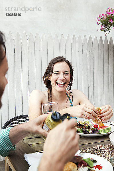 Glückliche Frau mit Freund beim Essen,  während sie im Hof am Tisch sitzt