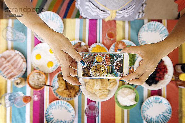 Ausgeschnittenes Bild von Frauenhänden beim Fotografieren von Essen bei Tisch