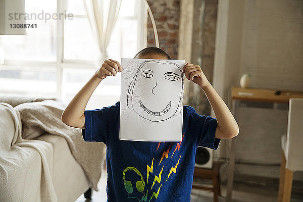 Junge zeigt Zeichnung,  während er zu Hause im Wohnzimmer steht