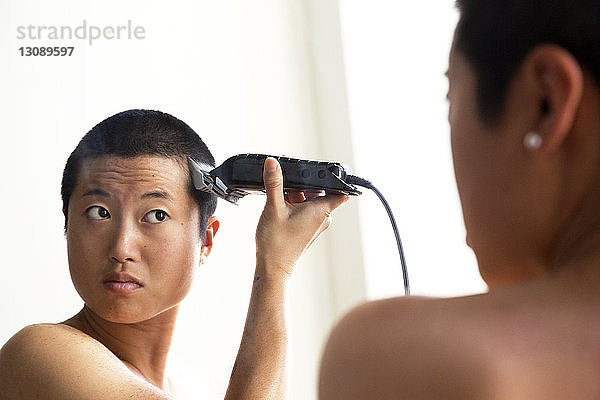 Frau rasiert sich die Haare,  während sie im Spiegel reflektiert