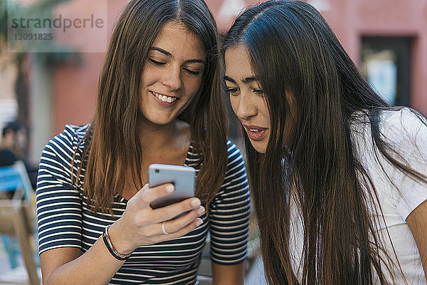 Freunde benutzen Mobiltelefon,  während sie im Straßencafé sitzen