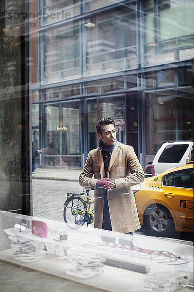 Mann steht auf Fußweg,  gesehen durch Fenster im Laden