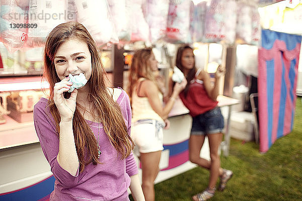 Porträt einer Teenagerin,  die mit Freunden im Hintergrund Zuckerwatte isst