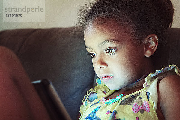 Nahaufnahme eines Mädchens,  das einen Tablet-Computer benutzt,  während es zu Hause auf dem Sofa sitzt