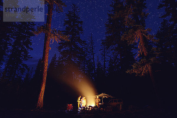 Menschen stehen nachts am Lagerfeuer auf einem Campingplatz im Wald