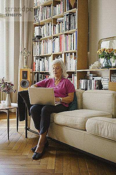 Ältere Frau mit Laptop auf dem Wohnzimmersofa