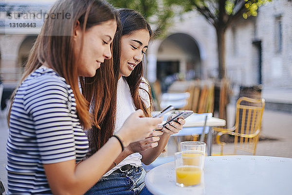 Freunde benutzen Mobiltelefone,  während sie im Straßencafé sitzen