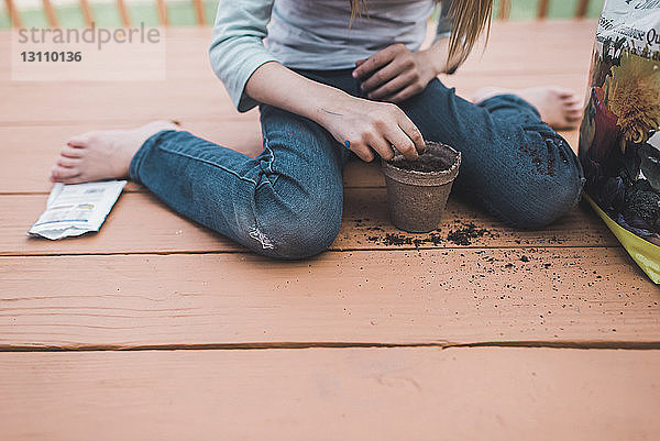 Unterer Teil eines Mädchens pflanzt Samen in einen Topf,  während es auf der Veranda sitzt