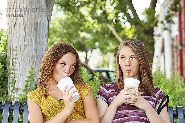 Freunde genießen ein Getränk,  während sie auf einer Parkbank sitzen