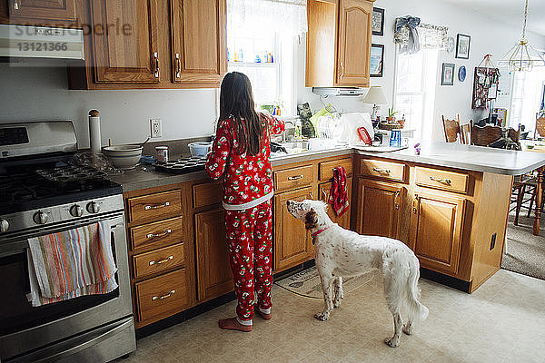 Rückansicht eines Mädchens,  das Essen zubereitet,  während es in der Küche beim Hund steht