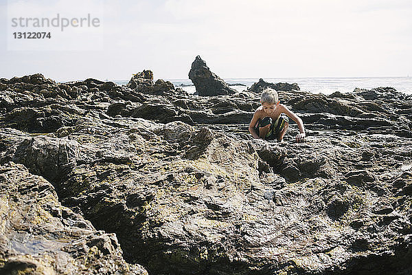 Junge spielt auf Felsen am Strand gegen den Himmel