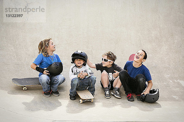 Fröhliche Jungen unterhalten sich,  während sie auf der Skateboard-Rampe sitzen