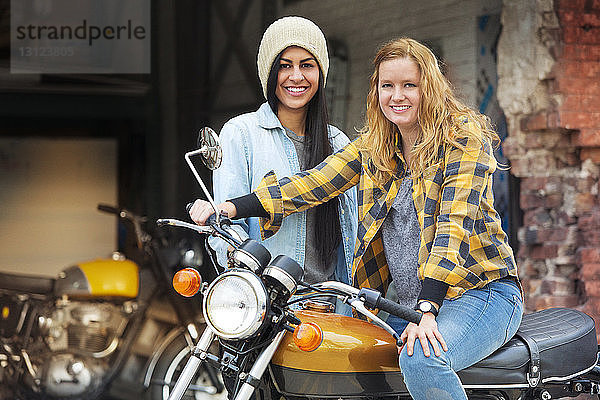 Porträt von fröhlichen Freundinnen mit Fahrrad vor einer Autowerkstatt