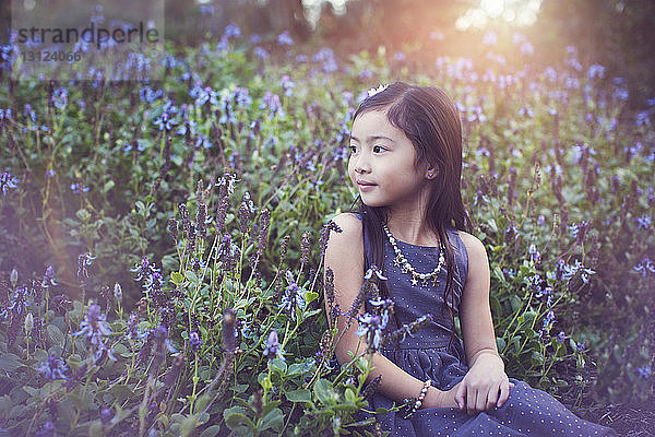 Süßes Mädchen schaut weg,  während es inmitten blühender Pflanzen im Park sitzt