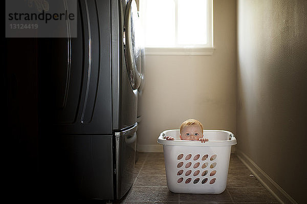 Porträt eines süßen kleinen Jungen im Wäschekorb bei der Waschmaschine