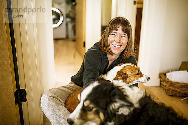 Porträt einer Frau mit Hunden,  die zu Hause auf dem Boden sitzt