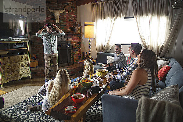 Glückliche Freunde schauen den Menschen an,  während sie beim geselligen Beisammensein zu Hause ein Heads-up-Spiel spielen