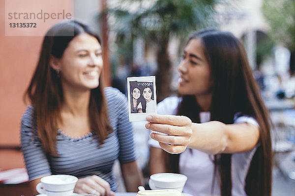 Frau zeigt Sofortfoto,  während sie mit einem Freund im Straßencafé sitzt