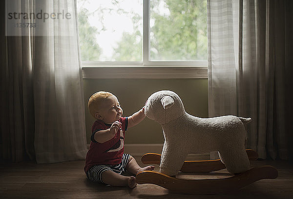 Kleiner Junge spielt mit Lammwippe,  während er zu Hause auf dem Boden sitzt