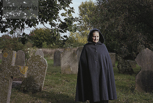 Traurige Frau im Mantel geht auf dem Feld auf dem Friedhof