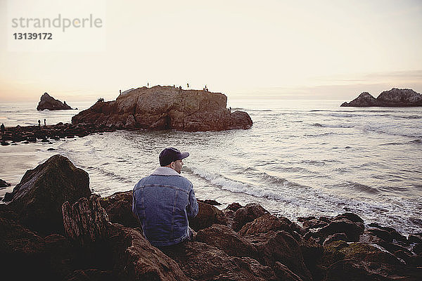 Rückansicht eines Menschen,  der sich auf Felsen am Meer gegen den Himmel entspannt