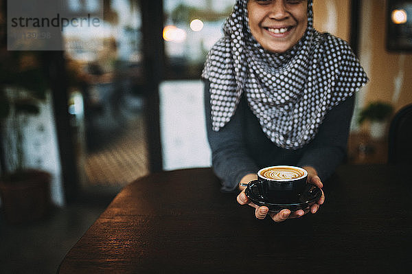 Lächelnde Frau in der Mitte,  die Kaffee hält,  während sie im Café sitzt