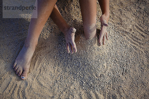 Niedriger Abschnitt eines Mädchens,  das am Strand mit Sand spielt