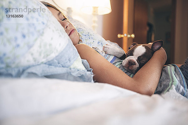 Mädchen liegt im Bett und hält Boston-Terrier-Welpen die Augen geschlossen
