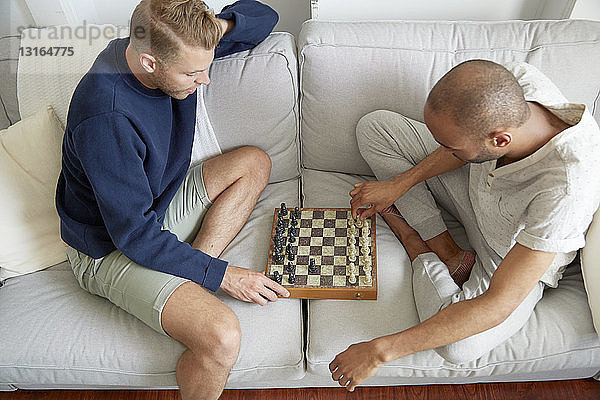 Hochwinkelansicht von Männern,  die lächelnd auf dem Sofa sitzen und Schach spielen