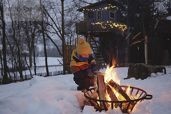 Junge sitzt am Feuer in verschneiter Landschaft