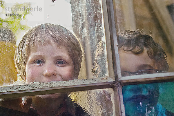 Porträt von zwei Jungen,  die durch ein Hüttenfenster schauen