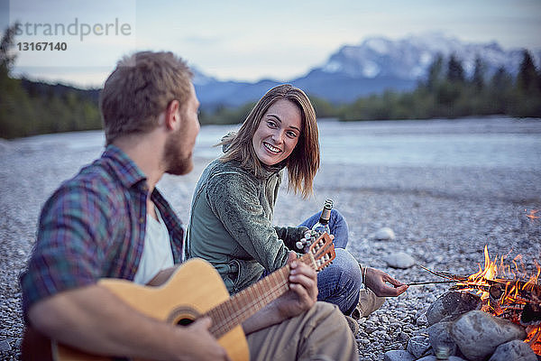 Junges Paar sitzt am Lagerfeuer und spielt Gitarre,  Wallgau,  Bayern,  Deutschland