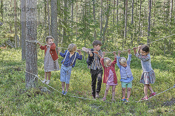 Mädchen und Jungen in Retro-Kleidung balancieren auf Seilen im Wald