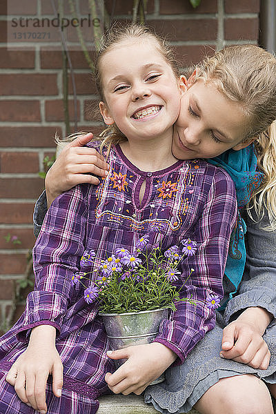 Zwei Schwestern mit Blumentopfpflanze im Garten