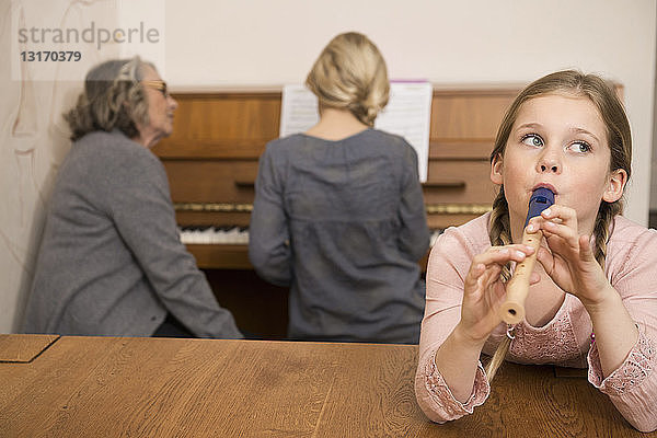 Mädchen spielt Blockflöte,  während die Schwester am Klavier von der Großmutter beobachtet wird