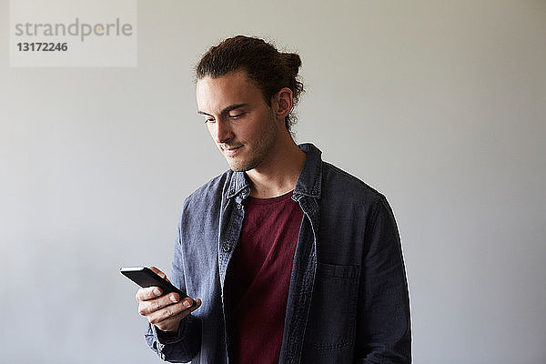 Kreativer Geschäftsmann mit Smartphone gegen graue Wand im Büro
