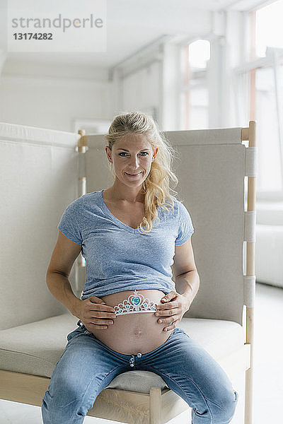 Porträt einer lächelnden schwangeren Frau,  die das Diadem am Bauch hält