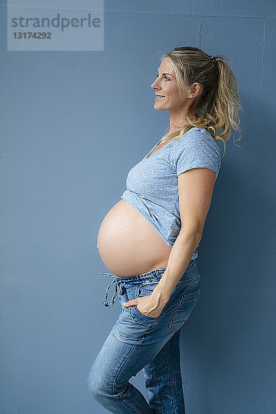 Lächelnde schwangere Frau steht an blauer Wand