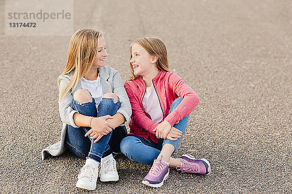 Zwei lächelnde Mädchen sitzen nebeneinander auf dem Boden