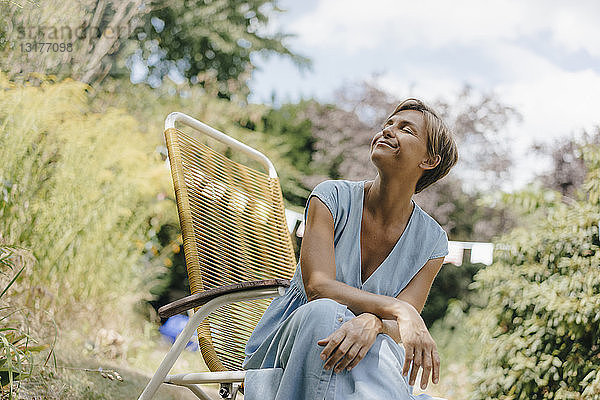 Entspannte Frau sitzt im Garten auf einem Stuhl mit geschlossenen Augen