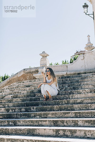 Spanien,  Valencia,  Frau sitzt auf einer Treppe und benutzt ein Smartphone