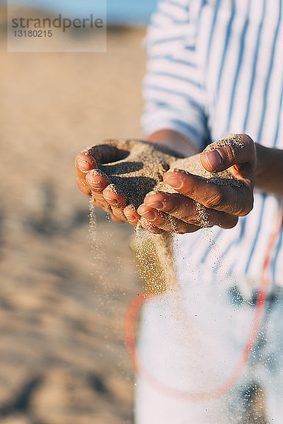 Frau am Strand,  die Sand durch ihre Hände rieseln lässt,  Nahaufnahme