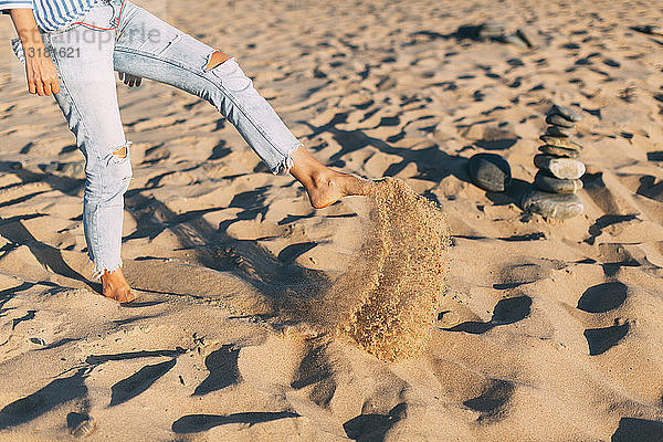 Frau steht auf einem Bein und wirft Sand an den Strand,  Teilansicht