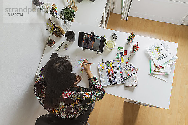 Illustratorin malt am Schreibtisch in einem Atelier mit einem digitalen Tablett,  Draufsicht