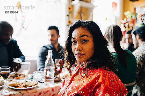 Porträt einer selbstbewussten jungen Frau,  die am Tisch gegen multi-ethnische Freunde sitzt,  die im Restaurant brunchen