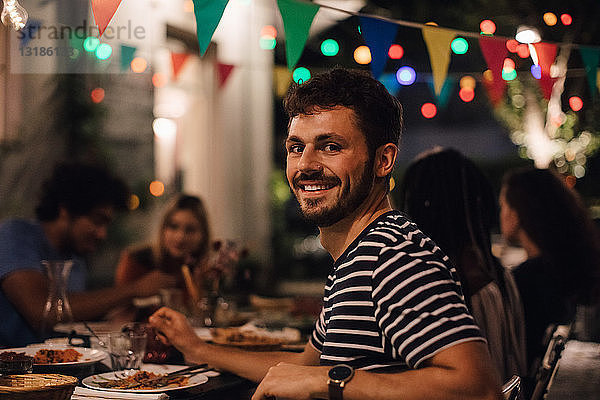 Porträt eines lächelnden jungen Mannes beim Abendessen mit Freunden während einer Gartenparty